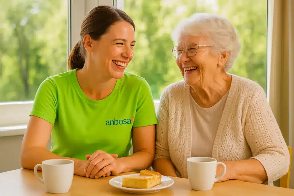 Herzlich lachende Pflegekraft mit Seniorin am Kaffeetisch in der anbosa Homecare Tagespflege Palisadenstraße in Berlin – jetzt auf die Warteliste setzen lassen.
