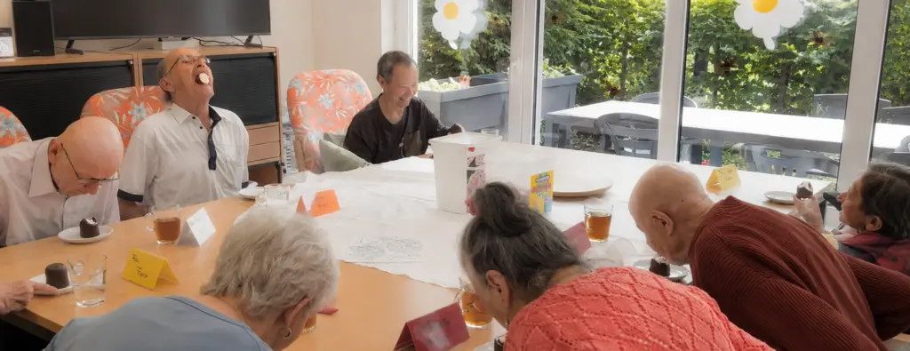 Spaß in der Tagespflege: Seniorinnen und Senioren nehmen an einem fröhlichen Schaumkusswettessen teil.