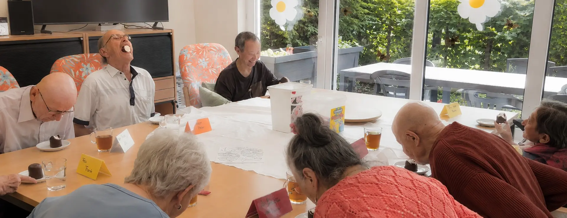 Spaß in der Tagespflege: Seniorinnen und Senioren nehmen an einem fröhlichen Schaumkusswettessen teil.