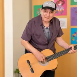 Ein älterer Gast der anbosa Tagespflege Palisadenstraße steht mit einer akustischen Gitarre in einem hellen Gemeinschaftsraum.